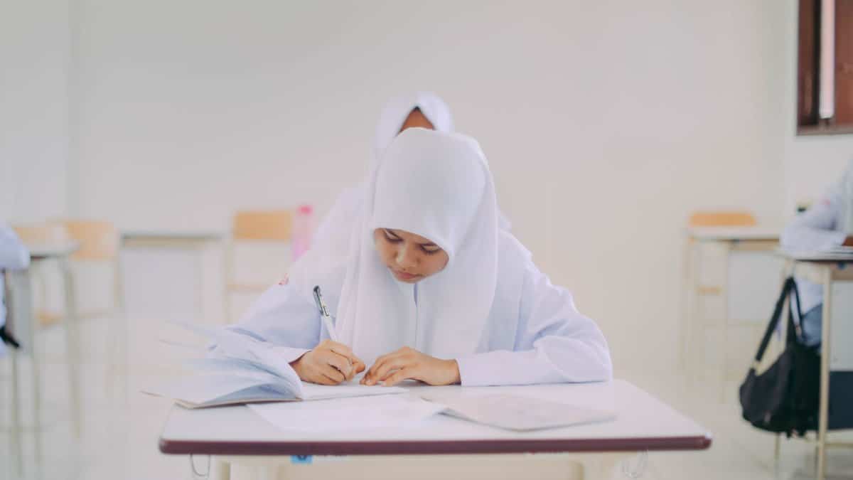 Muslim student focused on writing during class in Indonesia.