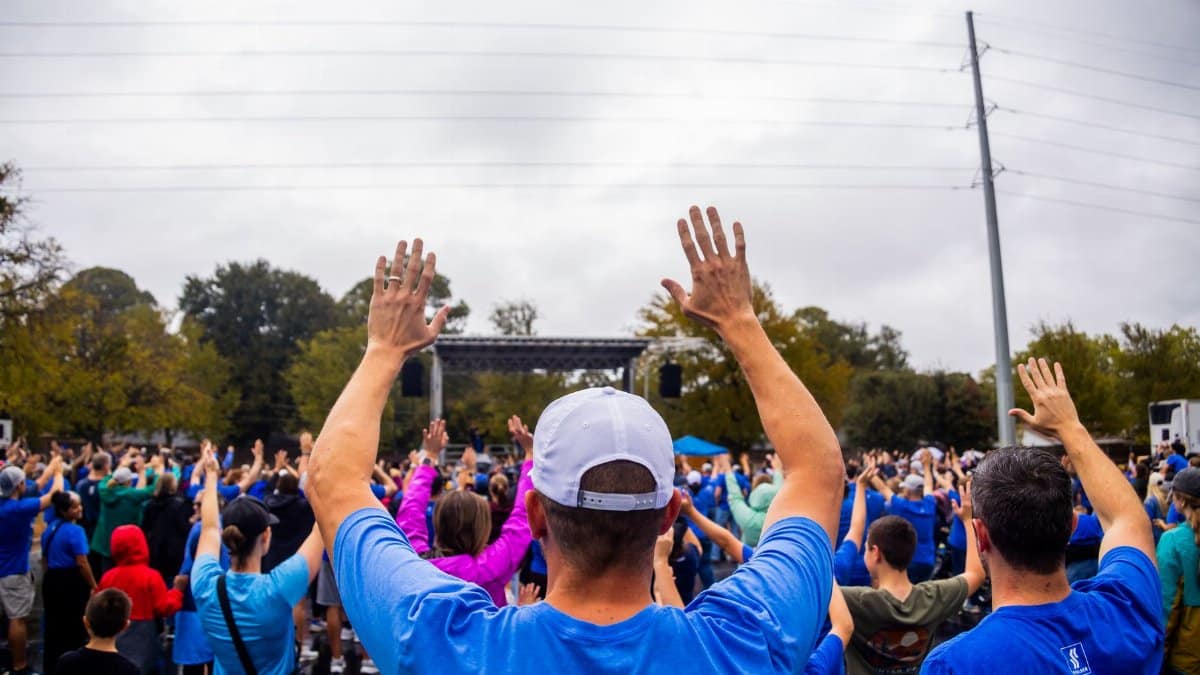 A large group of people raising their hands at an outdoor community event, creating a sense of unity and togetherness.