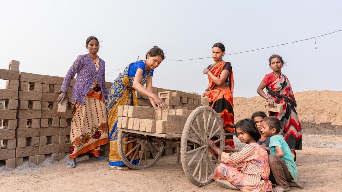 A group of women and children loading bricks onto a cart in a rural area, symbolizing community labor.