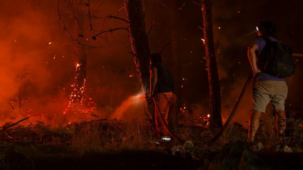 Dramatic scene of firefighters combatting a forest wildfire under dark, smoky skies.