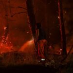 Dramatic scene of firefighters combatting a forest wildfire under dark, smoky skies.