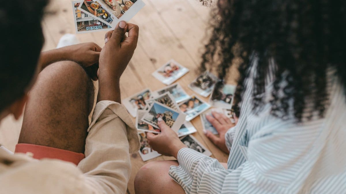 A couple sits together indoors reviewing a collection of printed photos, exemplifying nostalgia and shared moments.