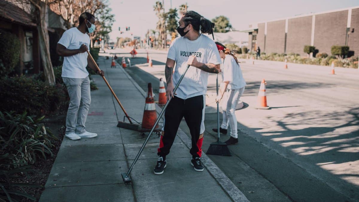 Volunteers wearing masks sweep an urban sidewalk, enhancing community and social good efforts.