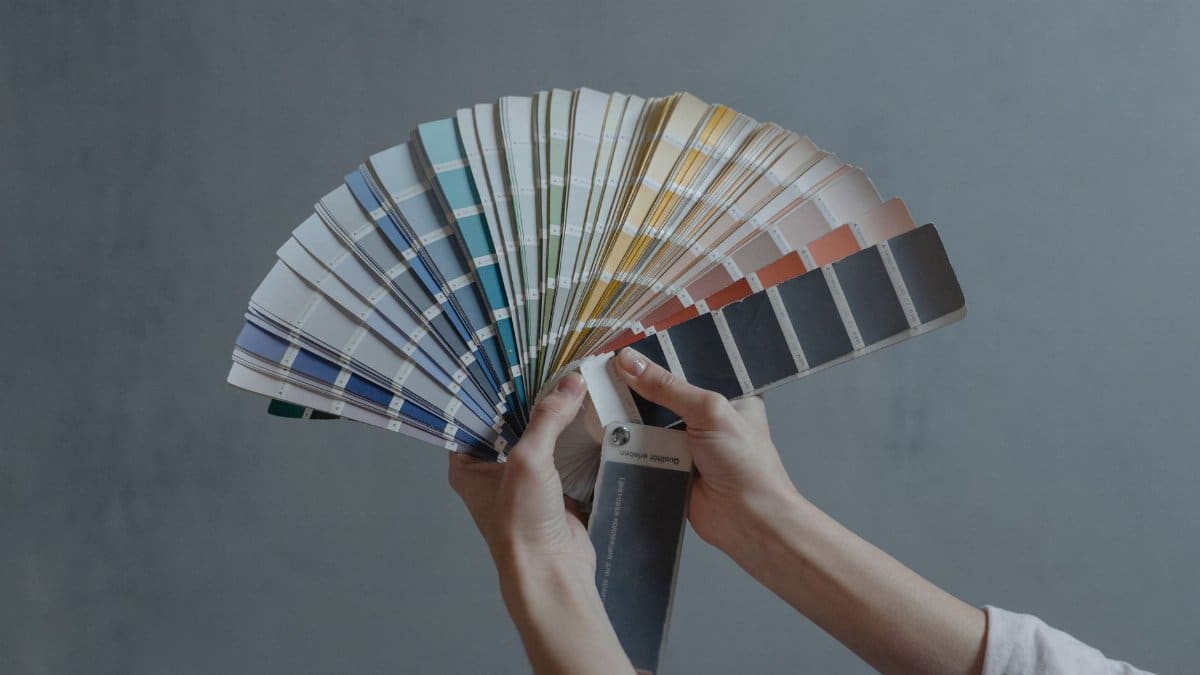 Hands holding a colorful fan of swatches on a gray backdrop, ideal for design themes.