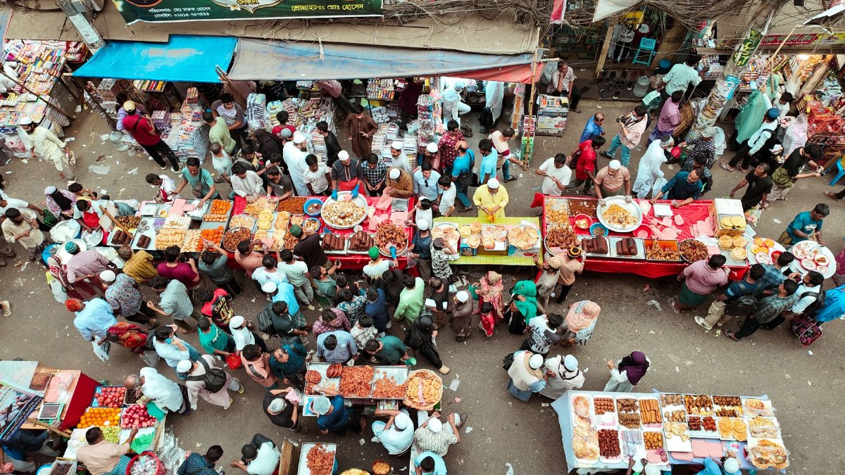 Busy street market with diverse food stalls and crowds from an overhead view.