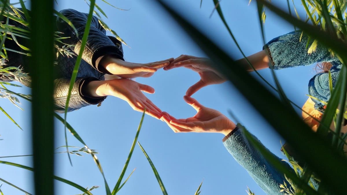 A unique perspective of hands forming a heart shape against a blue sky.