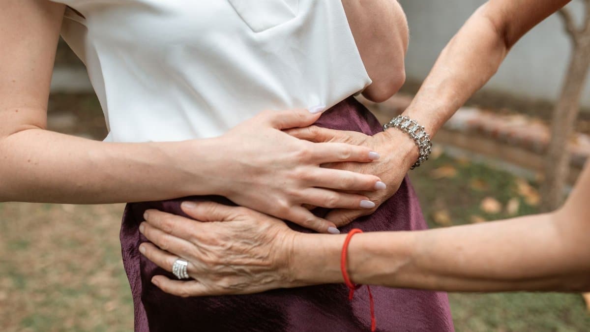 A close-up of multiple hands supporting a pregnant woman outdoors, symbolizing care and support.