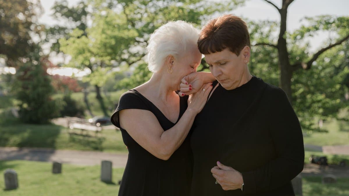 Two women embracing and grieving in an outdoor cemetery setting.