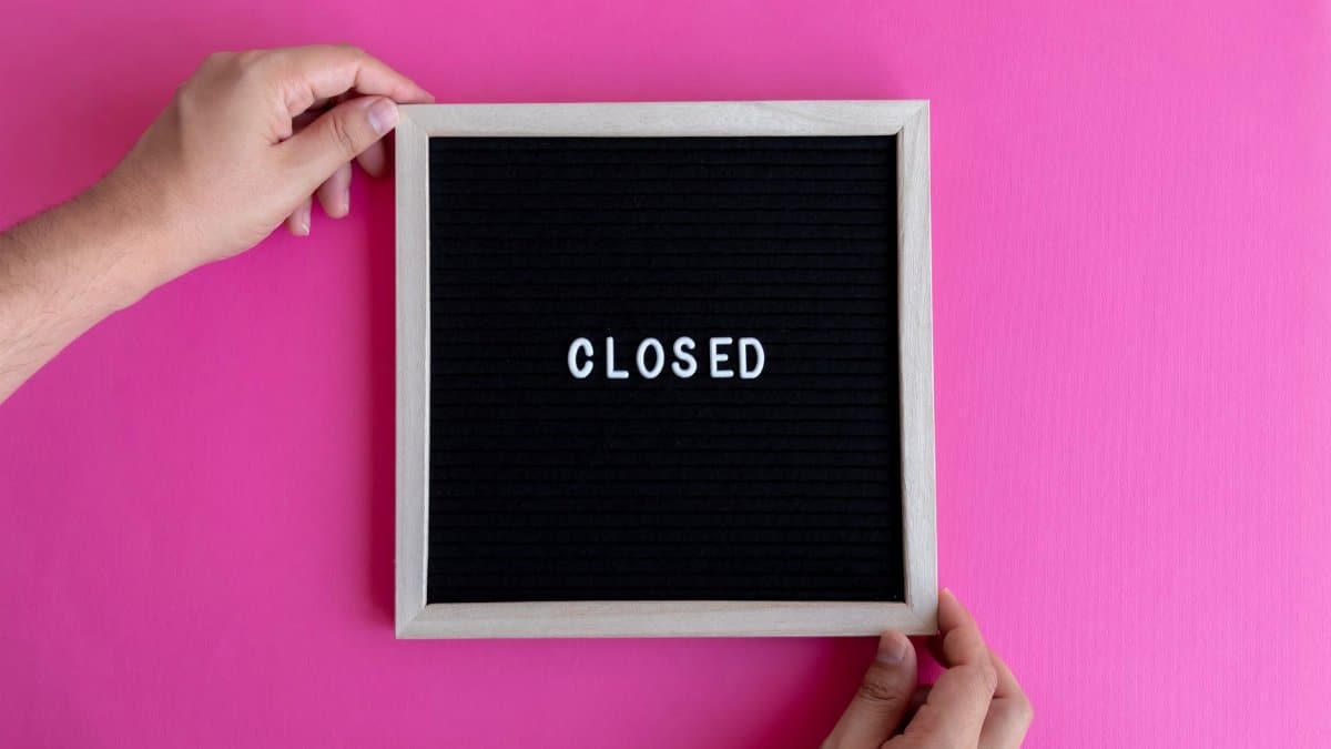 Hands holding a blackboard with 'Closed' text on a vibrant pink background, conveying closure or unavailability.