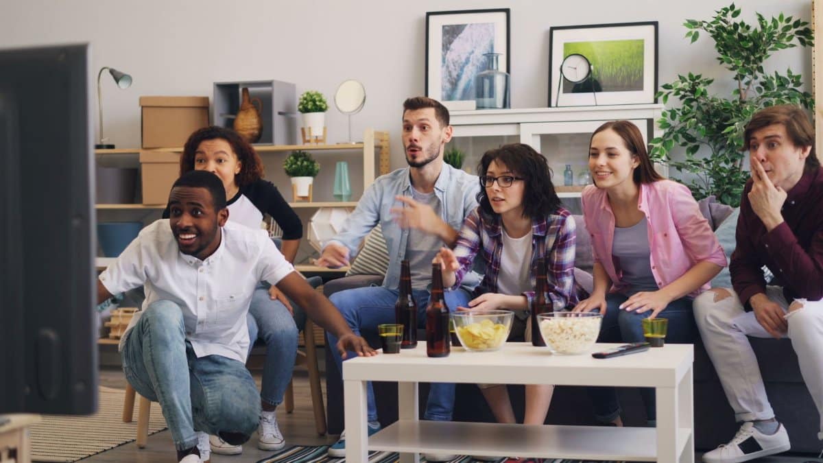 A diverse group of friends excitedly watching TV together in a modern living room setting.