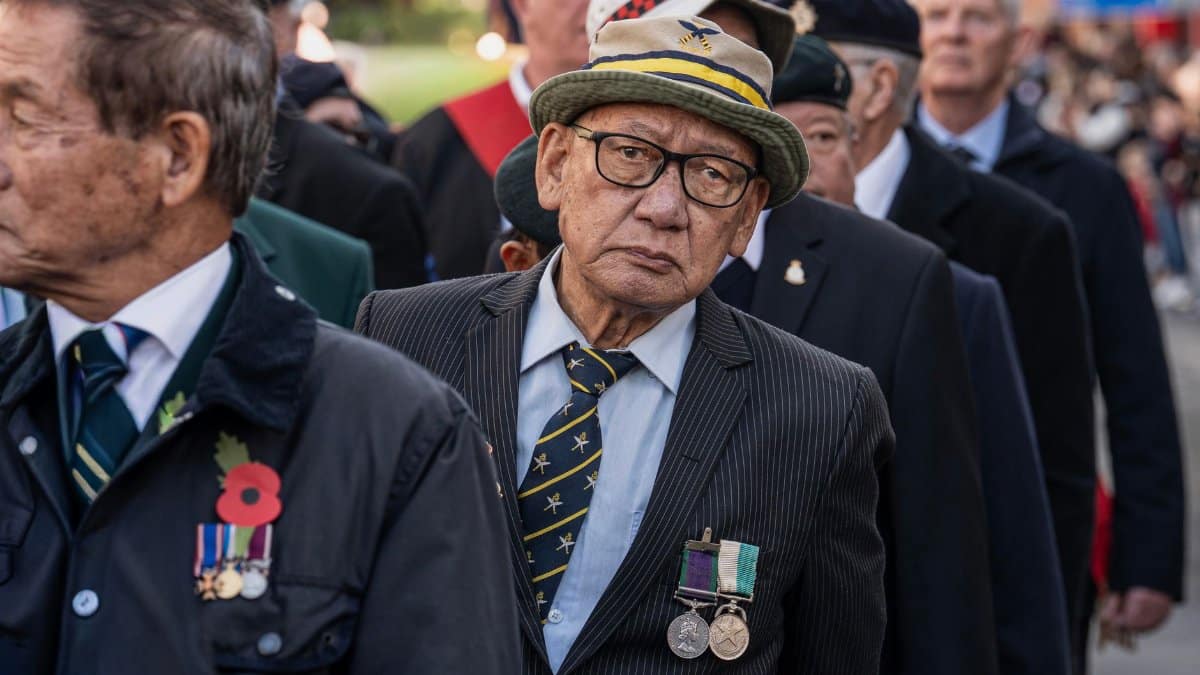 Group of elderly veterans marching in a Remembrance Day parade outdoors.