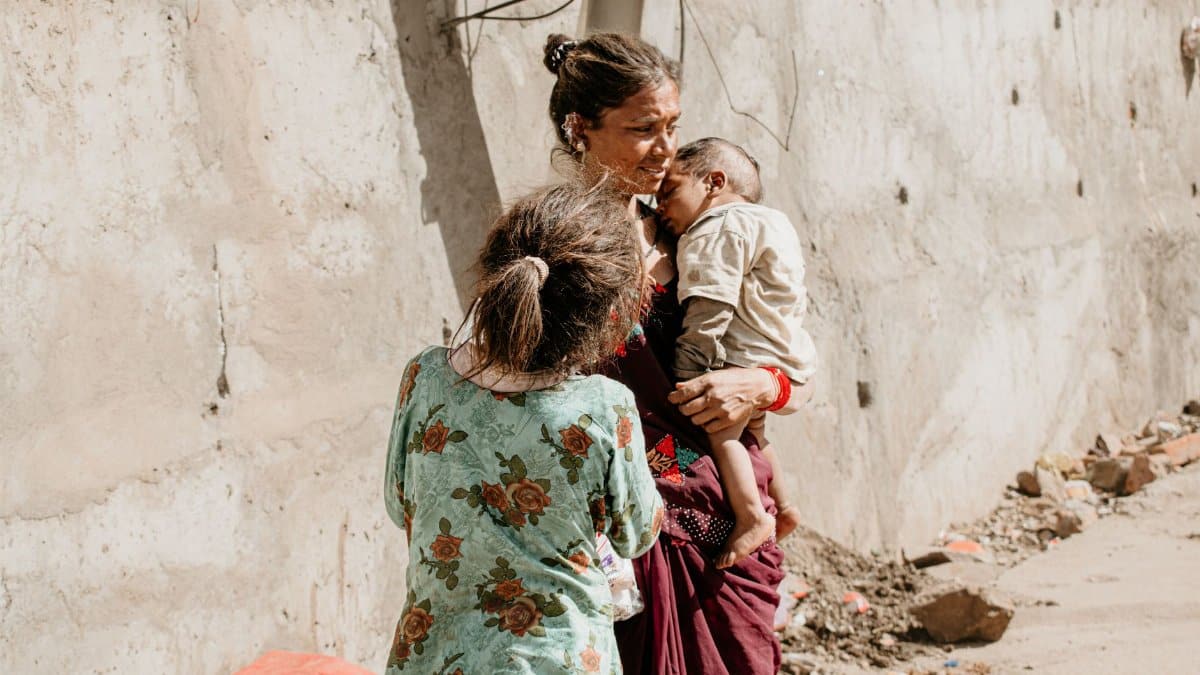 A mother holding her children on a sunlit street in Ujjain, India.