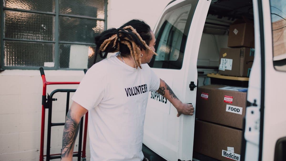 Volunteer loading boxes labeled food and medicine into van, supporting community donations.