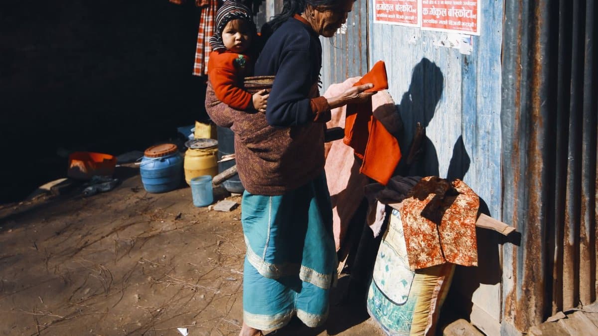 A woman carries a child in an urban setting, engaging in daily chores outdoors.