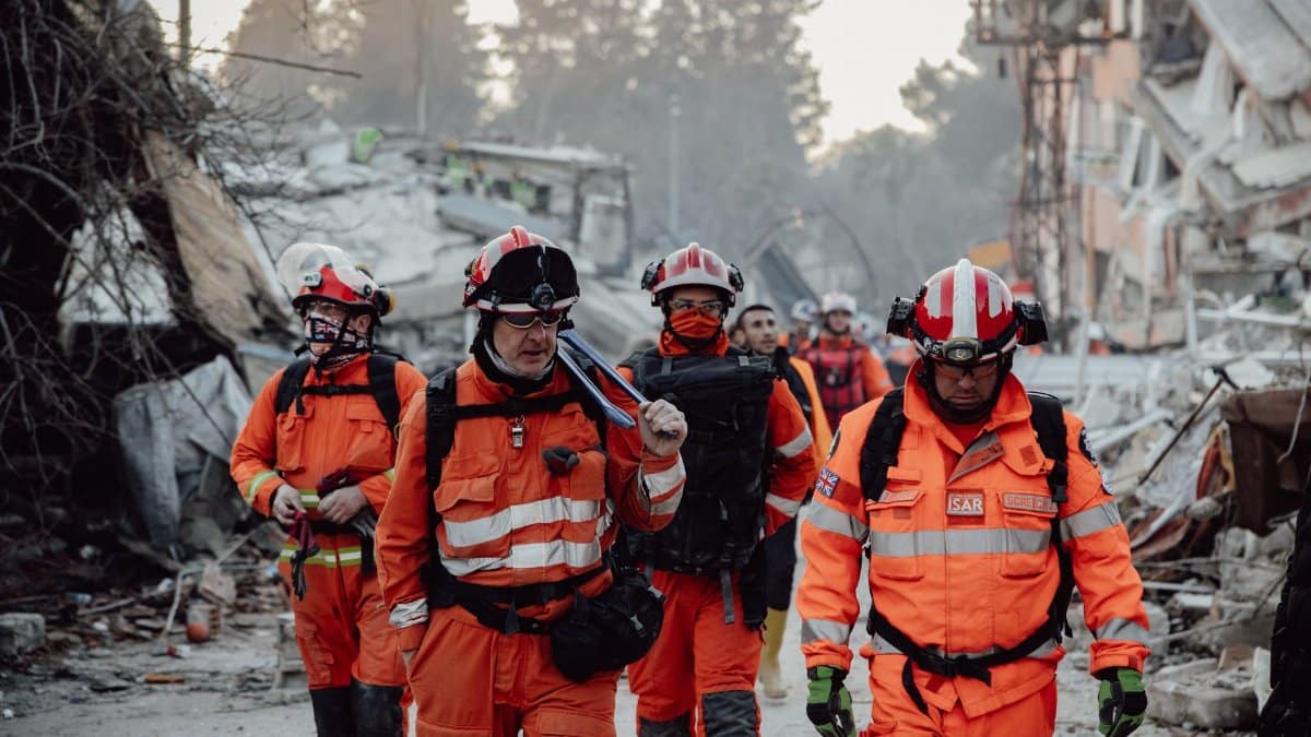 Search and rescue team in orange uniforms in a demolished area, assessing damage and carrying out operations.
