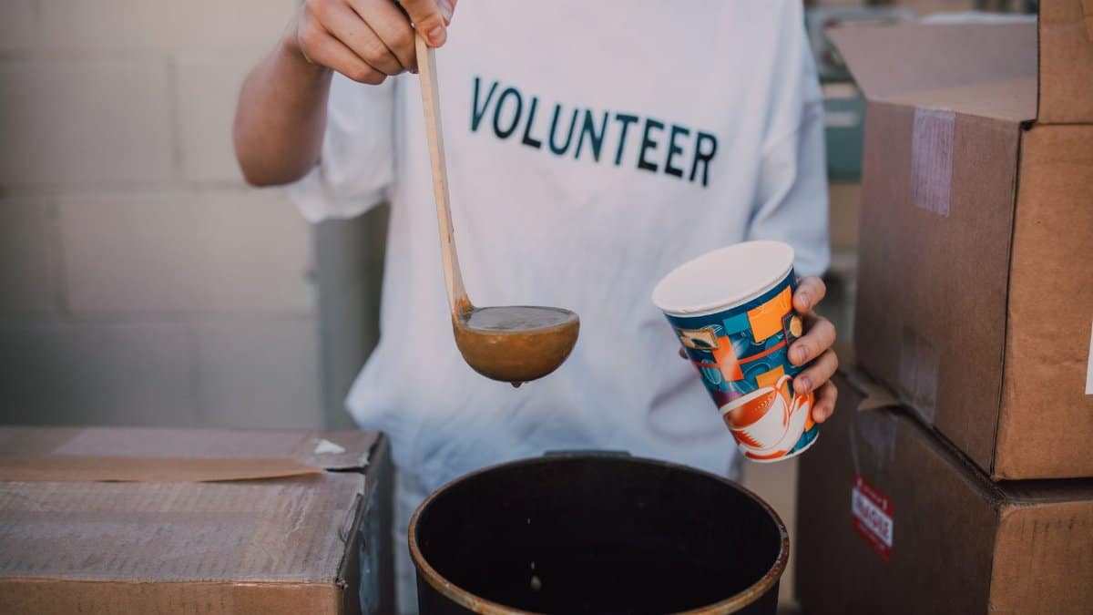 A volunteer in a t-shirt serving soup at a community event. Helping hand.