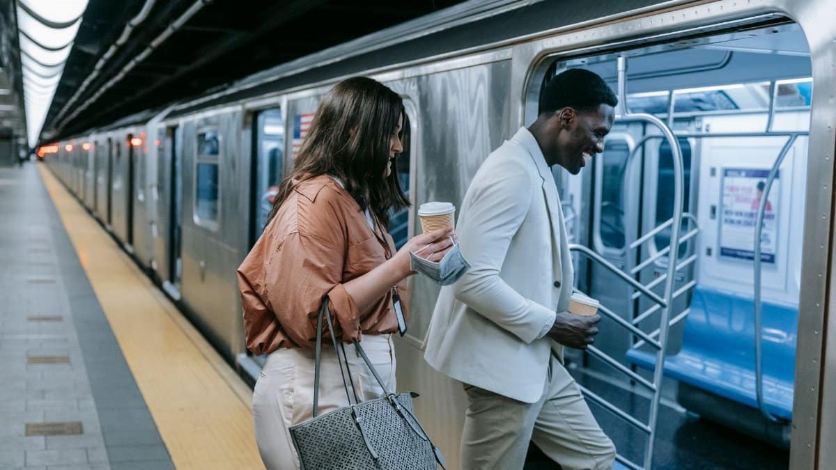 Two adults chatting and entering a train with coffee at a subway station.
