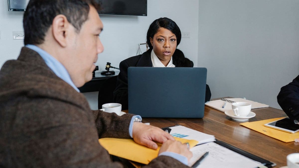 Group of multiethnic coworkers in formal wear sitting at table with laptop and documents while discussing business issues