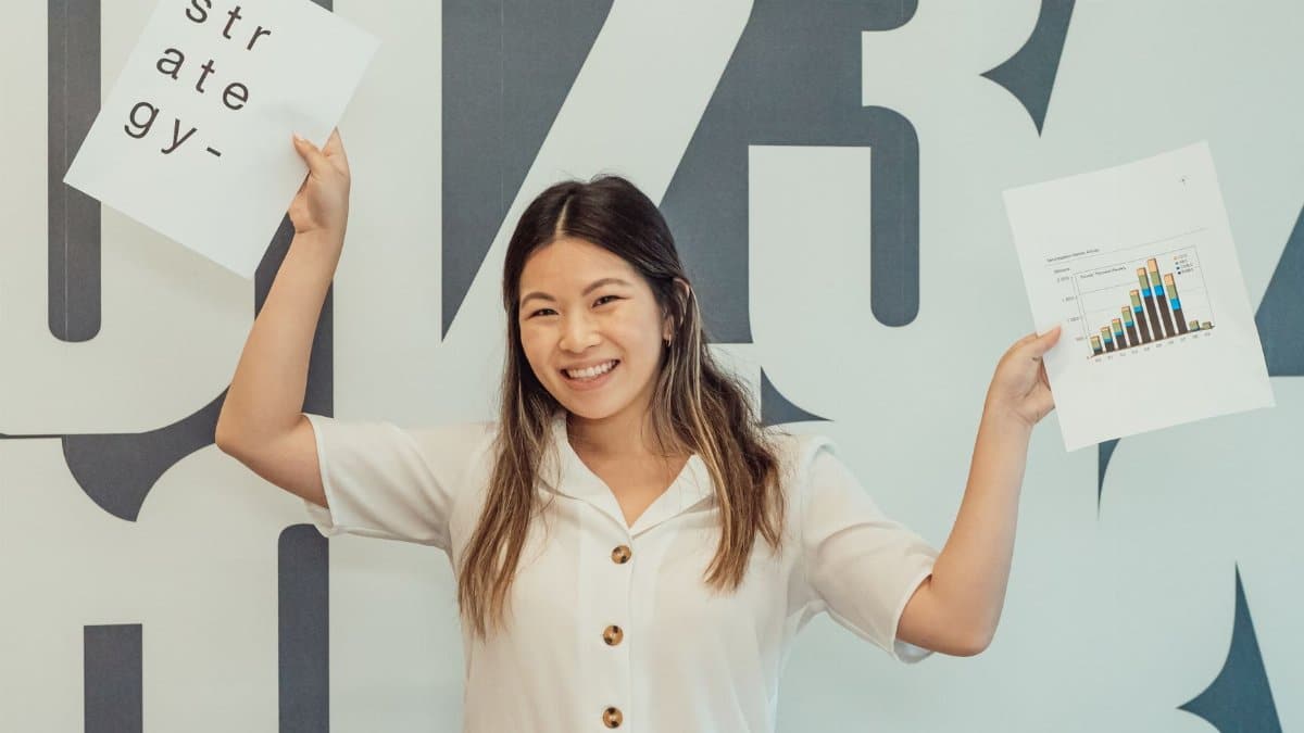 Smiling young woman in office holding business strategy documents, embodying enthusiasm and growth.