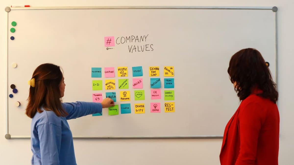 Two women in an office discussing company values on a whiteboard.