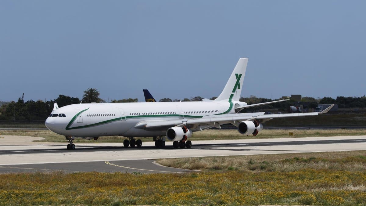 Wide-body aircraft with green accents taxiing on airport runway under clear sky.