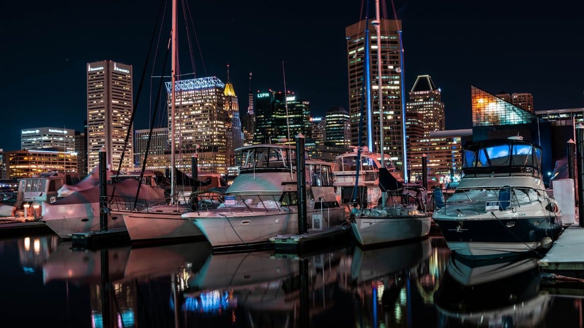 Baltimore skyline illuminated at night with yachts docked in the marina, reflecting urban luxury.