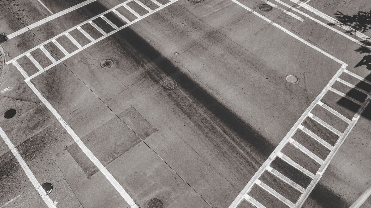 Monochrome aerial image of an empty urban crossroad with distinct pedestrian markings.