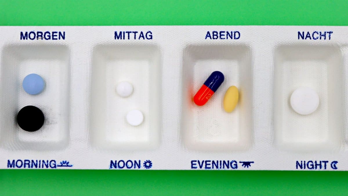 A daily medication organizer with pills for different times, set against a green backdrop.