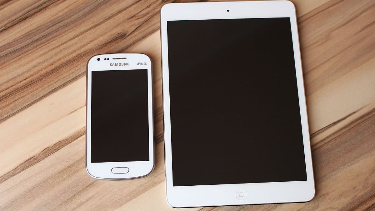 A white smartphone and tablet placed on a wooden table, showcasing technology contrast.