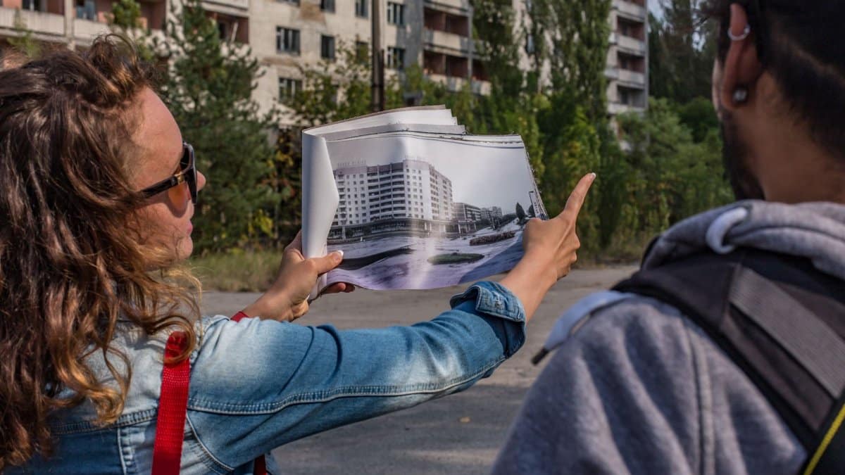 A woman shows an urban explorer a photo map in a decaying city setting.