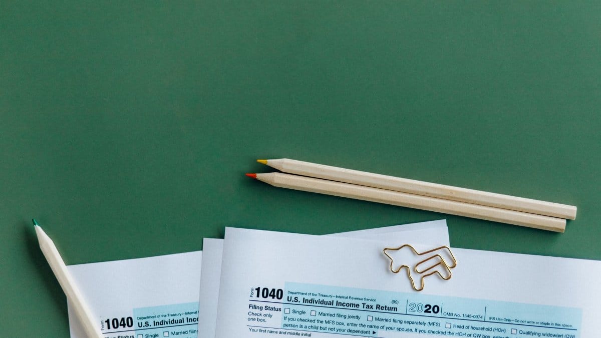 1040 tax form with colored pencils and paperclip on green background.