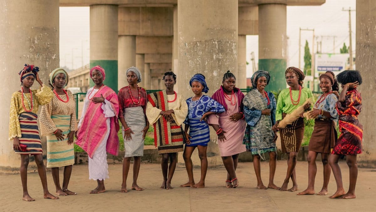 A group of women in vibrant traditional African attire pose under a bridge.