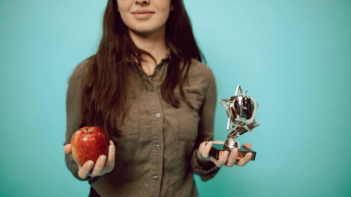 Woman holding an award trophy and apple against a turquoise background, symbolizing achievement and balance.