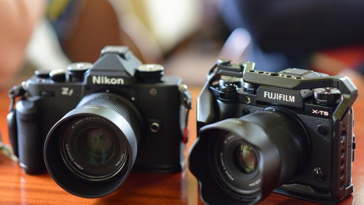 Close-up of Nikon and Fujifilm cameras on a wooden table, focusing on lens details.