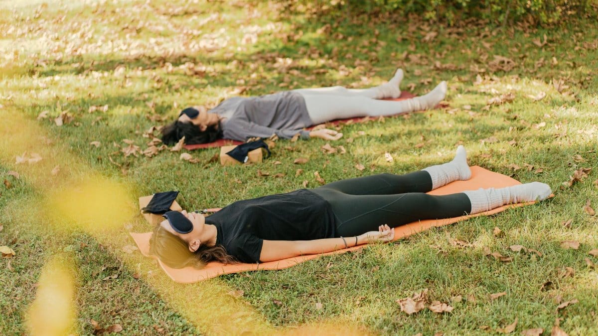 Two women practicing yoga and meditation on grass, focusing on relaxation.