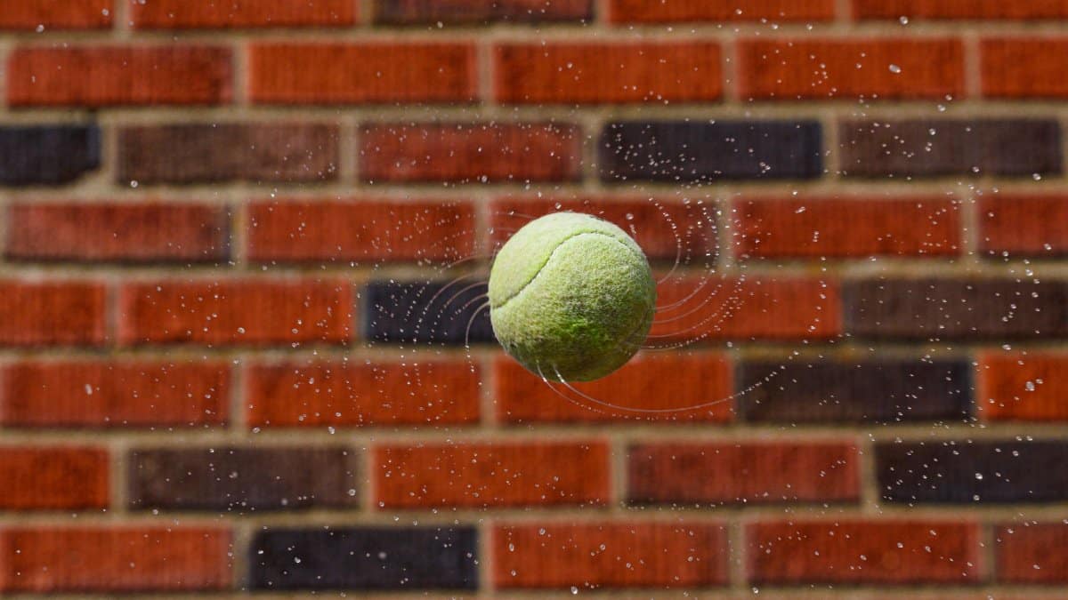 Dynamic tennis ball captured mid-air with water droplets and brick wall backdrop.
