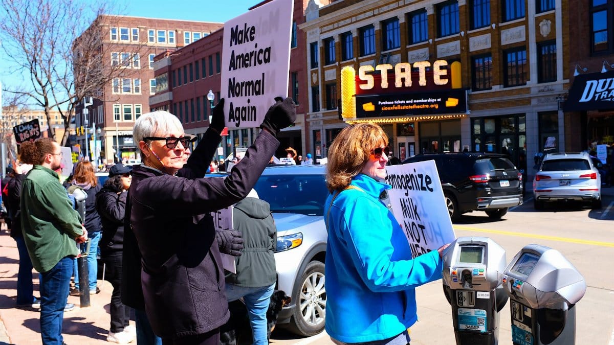 People protesting outside a small town theater with signs about social issues.