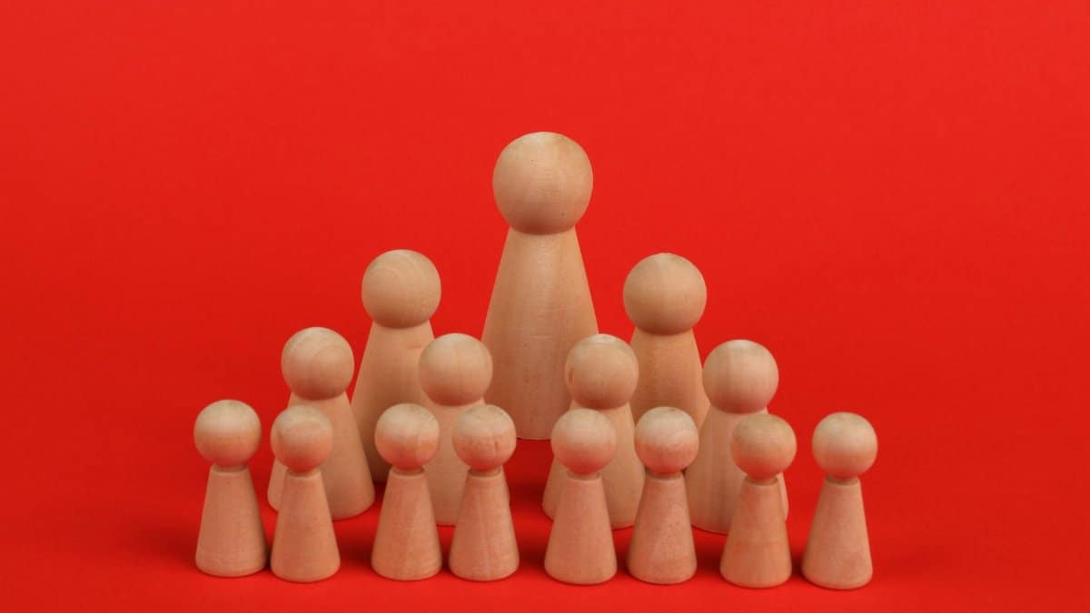 Wooden figurines arranged in hierarchy against bright red backdrop symbolizing leadership.