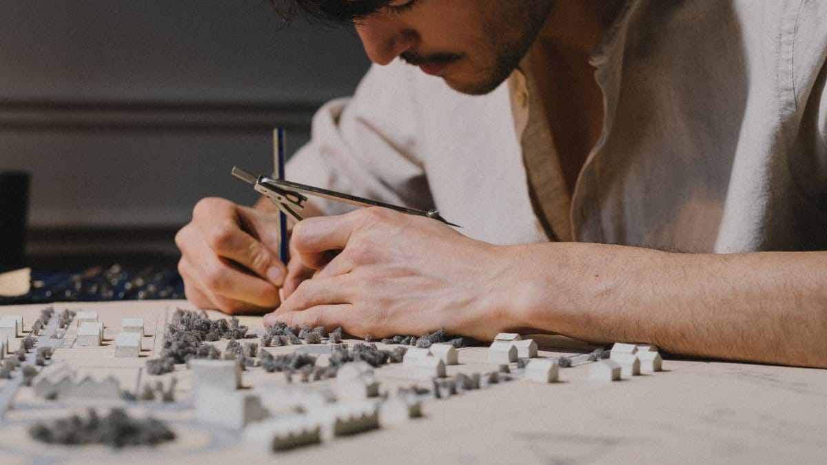 Architect focused on creating a detailed model using a compass indoors, showcasing precision and creativity.