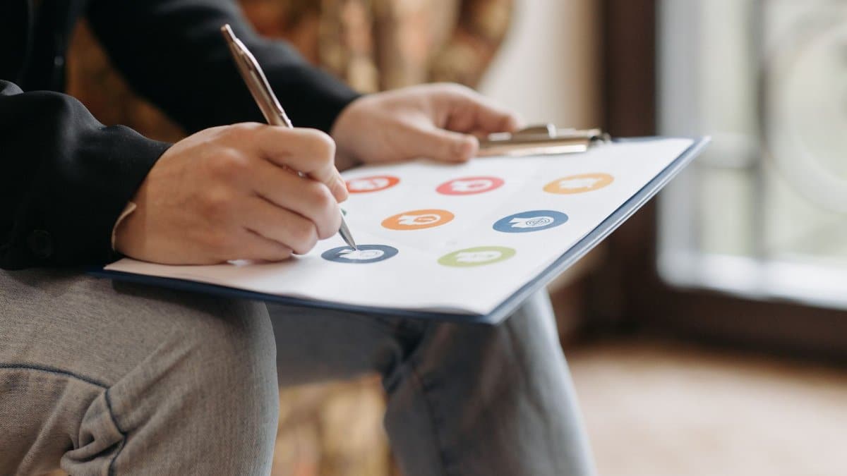 Close-up of a person writing on a clipboard with colorful icons.