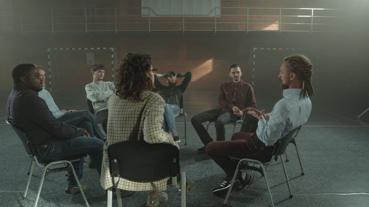 A diverse group engages in a therapy session inside a gym, fostering mental health support.