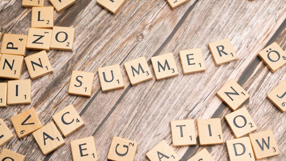 Scrabble tiles spelling 'SUMMER' on a rustic wooden surface, evoking warmth and creativity.