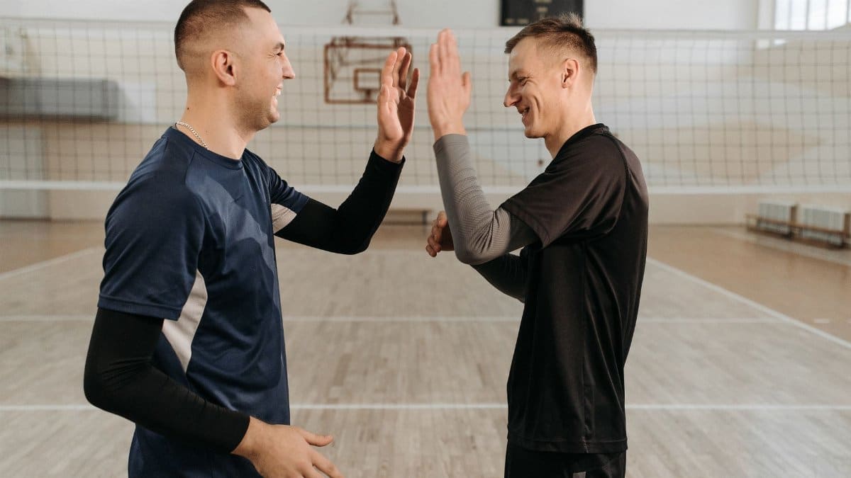 Two male volleyball players in sports uniforms high five on an indoor court.