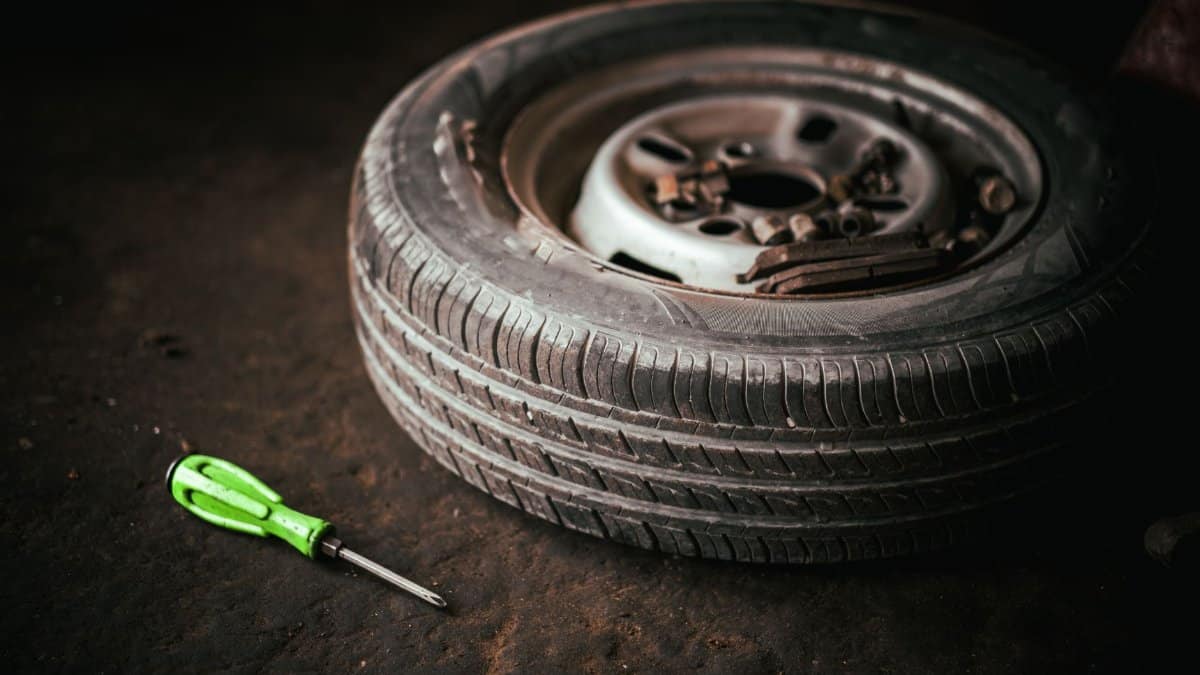 A car tire and green screwdriver placed on the garage floor, representing automotive repair.