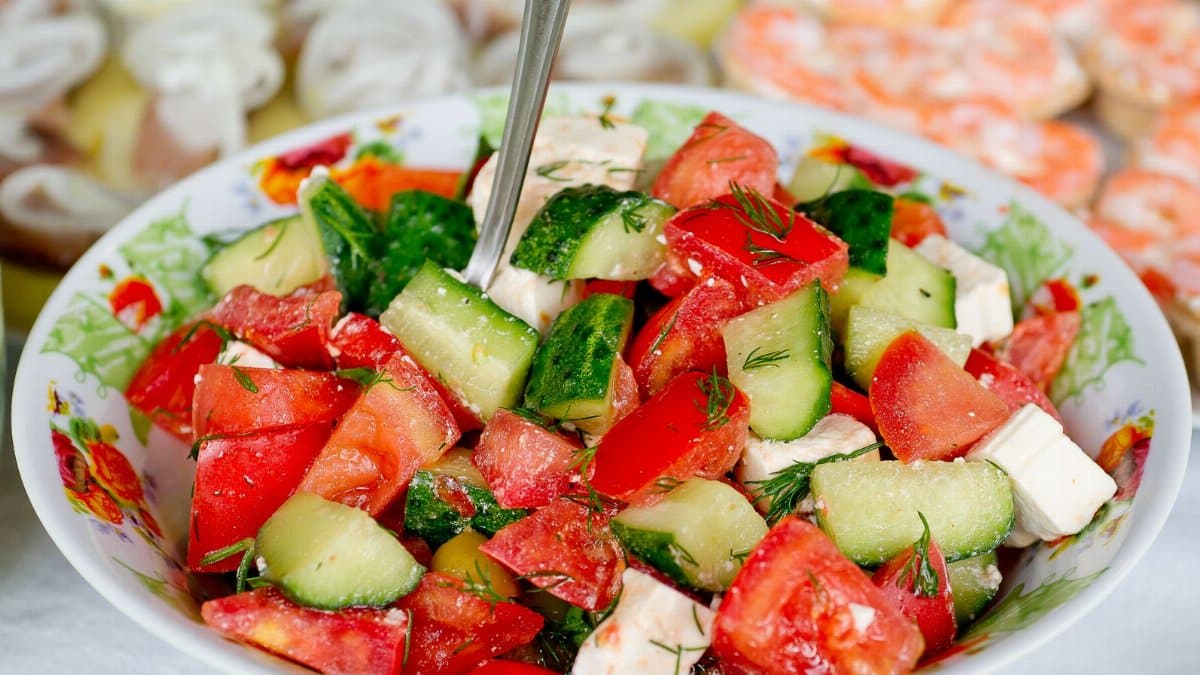 Salad of fresh cucumber and tomatoes mixed with cheese and parsley on table in bright room