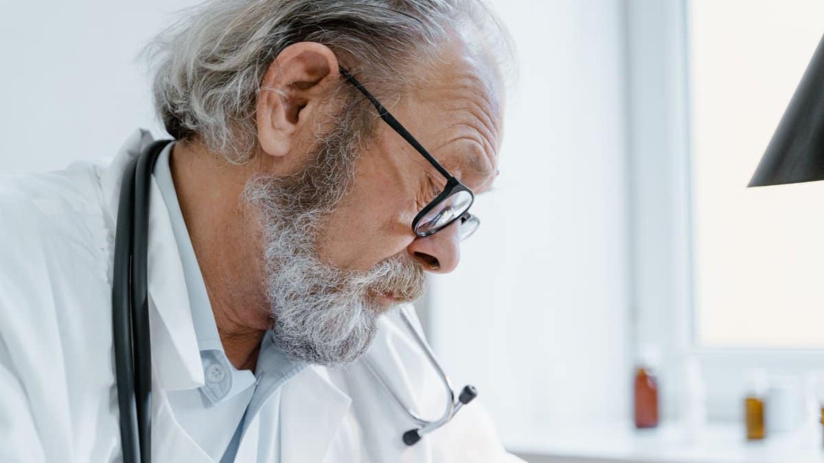Senior doctor with glasses and stethoscope focused on work in a medical office.