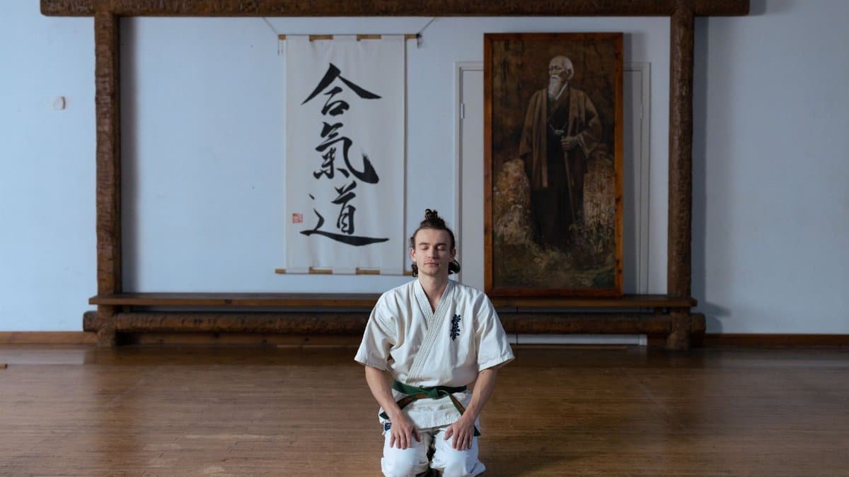 A man in traditional martial arts attire meditates peacefully in a dojo, emphasizing mindfulness.