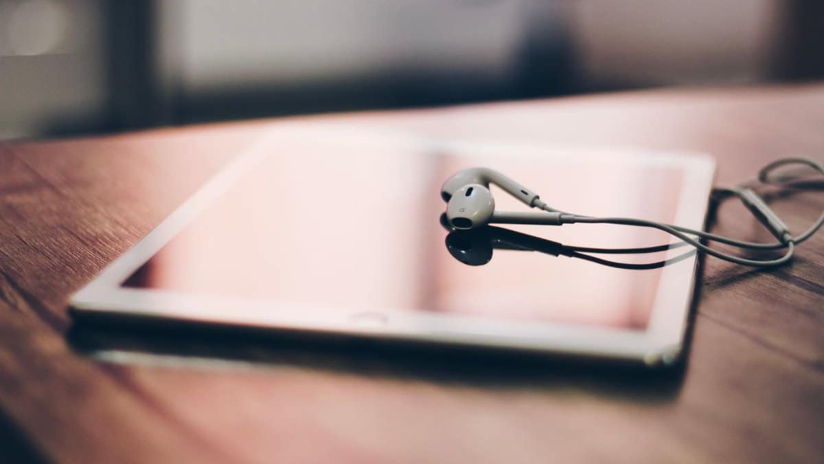 A tablet with earphones rests on a wooden surface, highlighting modern technology and connectivity.