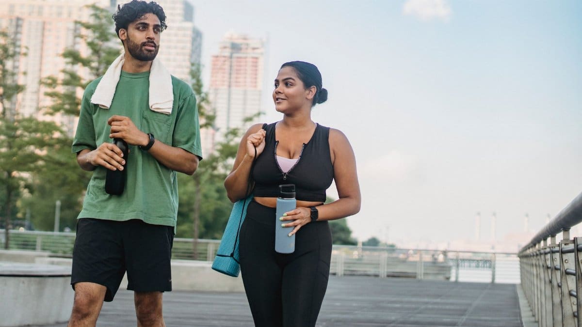 Two people in activewear walk with water bottles on a city boardwalk, promoting a healthy lifestyle.