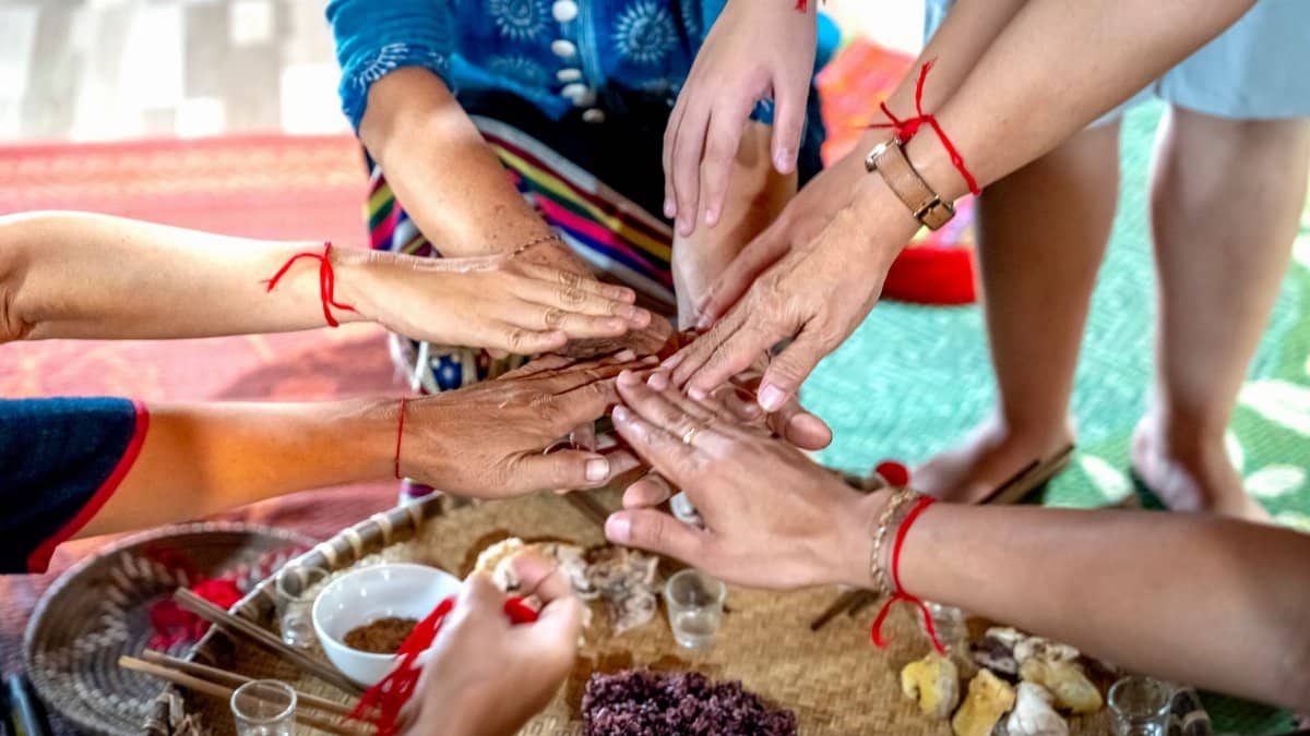 Hands with red bracelets gather over ritual items in a cultural celebration.